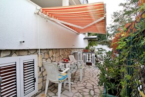 A patio with stone flooring, white furniture, and a striped canopy.