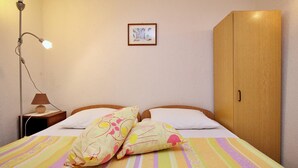 Un dormitorio con cama, almohadas, mesita de noche, lámpara, armario y un cuadro en la pared.