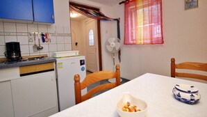 Cocina compacta con refrigerador, cafetera y comedor con mesa y sillas.