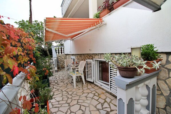 A patio with a stone floor, a white chair, a small table, and a potted plant.