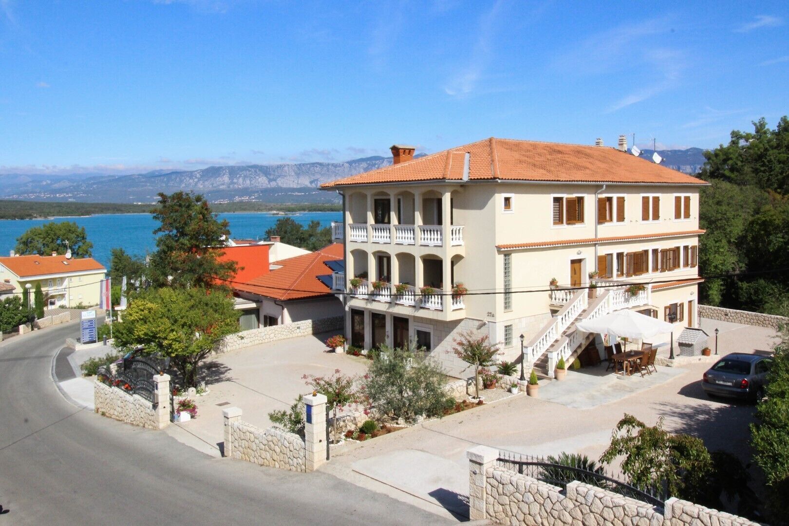 A two-story building with a balcony, a stone wall, and a view of the sea.