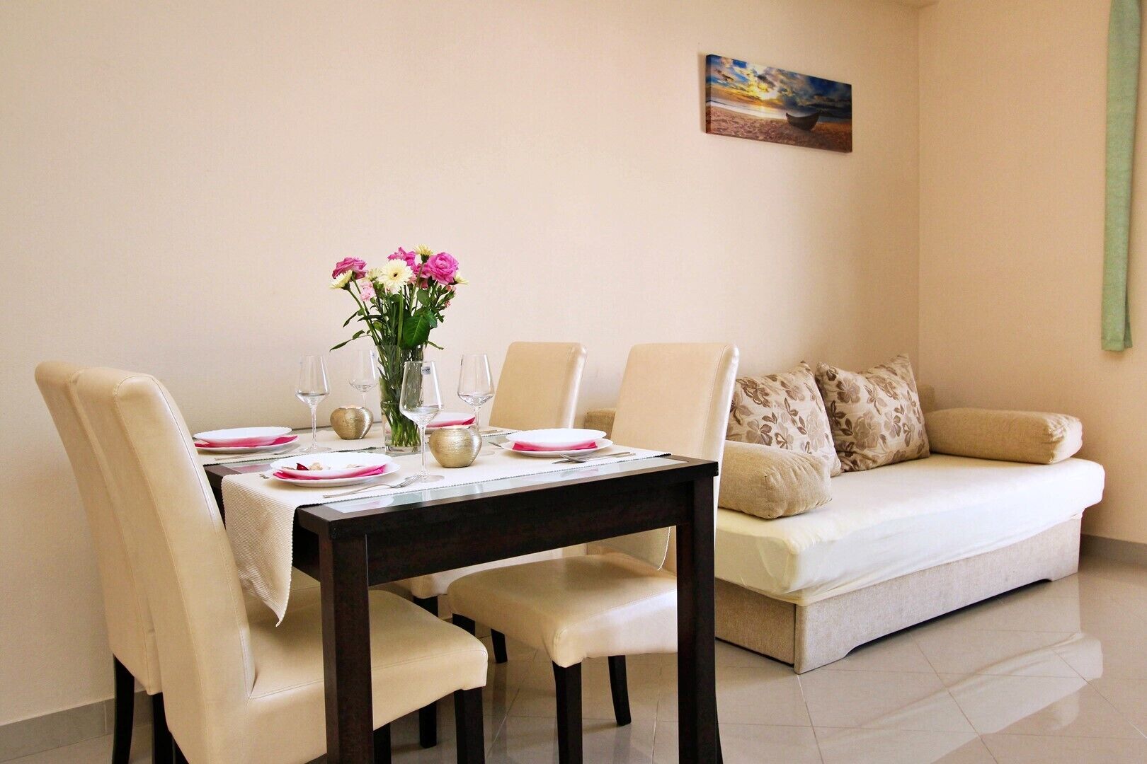 A dining area with a table set for four, a vase of flowers, and a painting on the wall.