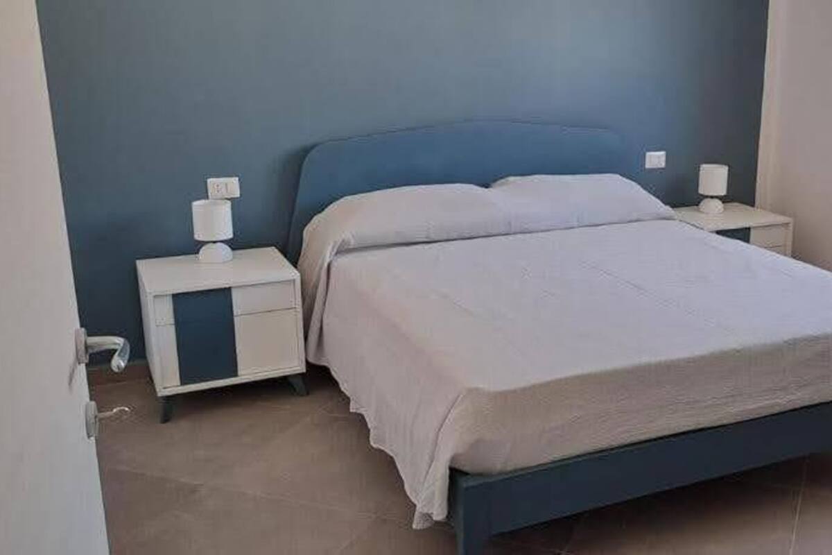 Un dormitorio con cama, mesitas de noche y ventana.