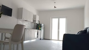 A modern kitchen with white cabinets, a dining area with a white table and chairs, and a large window providing natural light. - Tenuta Nonna Peppa Luxury apartment (Centola)