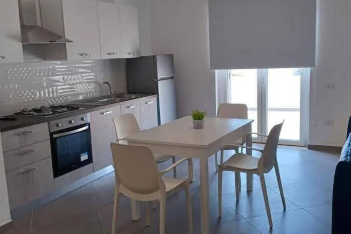 Una cocina moderna con armarios blancos, una mesa de comedor con sillas y un sofá azul en una sala de estar luminosa.