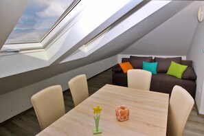 Um apartamento loft moderno com claraboia, mesa de jantar de madeira e sofá escuro com almofadas coloridas.