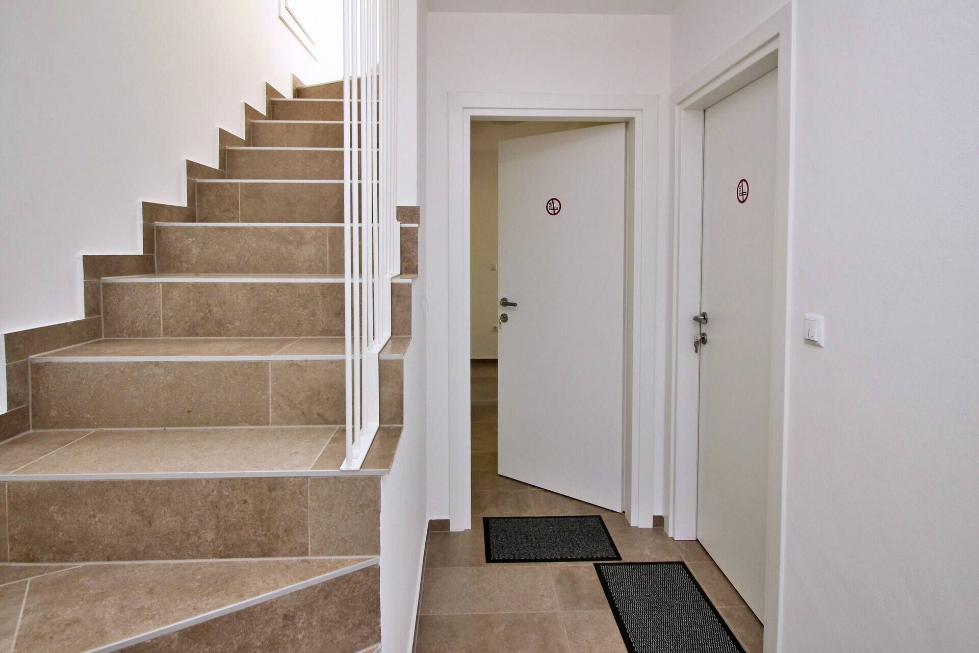 A staircase with beige tiles and white railings leading to a door with a doormat.