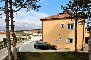 Um edifício de dois andares com telhado de telhas, um carro estacionado e árvores ao redor.