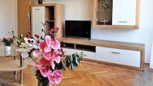 Een moderne woonkamer met een houten tv-meubel, een flatscreen televisie en een vitrinekast met glazen deuren.