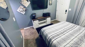 Een slaapkamer met een bed, een televisie, een koffiezetapparaat en kunst aan de muur.