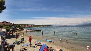 Een strand met mensen die zwemmen en zonnebaden, tenten en strandstoelen.