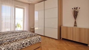 Une chambre à coucher comprenant un lit, une armoire, une table de chevet avec un vase, et donnant sur l’extérieur.