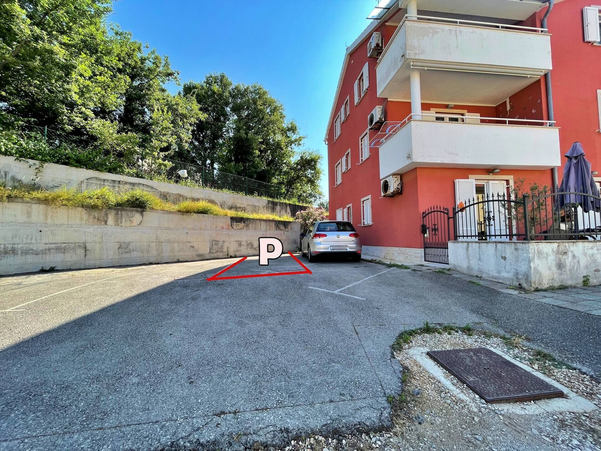 Une zone de stationnement avec une place de stationnement délimitée, une barrière en béton et un bâtiment rouge doté de balcons.