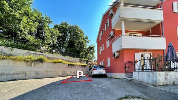 Une zone de stationnement avec une place de stationnement délimitée, une barrière en béton et un bâtiment rouge doté de balcons.