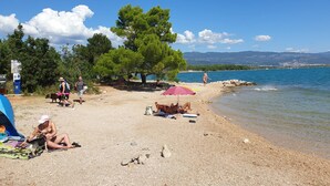 Une plage animée, avec des gens, des tentes et une vue dégagée sur la mer et les montagnes.