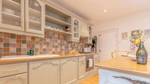 A kitchen with a tiled backsplash, wooden countertop, and a bottle of wine on the table.