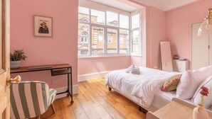 A bedroom with a bed, a desk, a chair, a window, and a view of buildings outside.