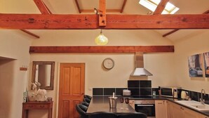 Una cocina con vigas de madera a la vista, una mesa de comedor con sillas, un reloj y un microondas.