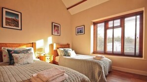 Un dormitorio con dos camas, cabeceros de madera y un ventanal con persianas.