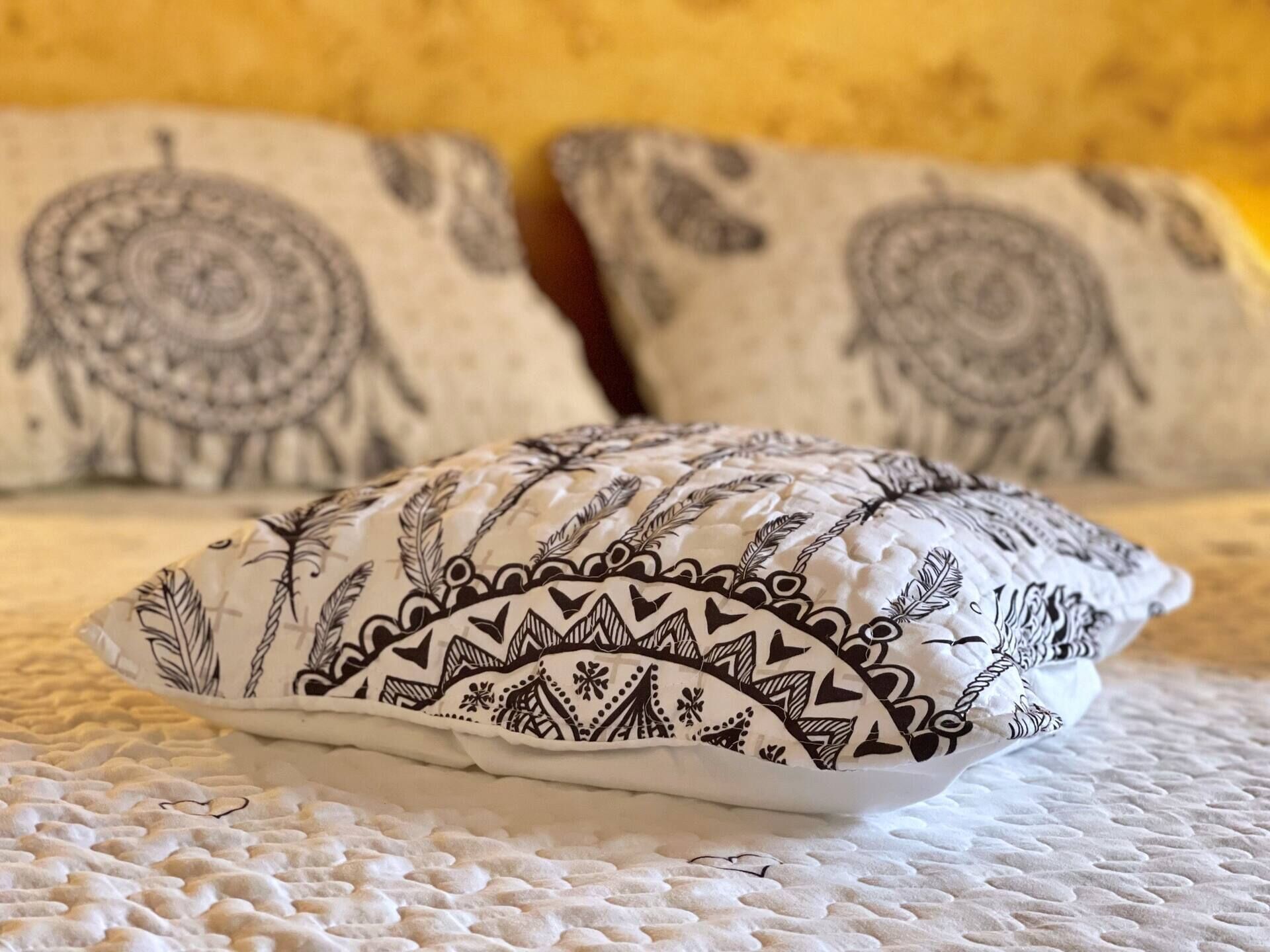 A bed with a white textured bedspread and two pillows with black and white patterns.