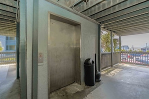 A covered outdoor area with a metal door, a trash bin, and a railing.