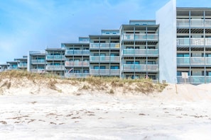 A beachfront hotel with multiple balconies and a sandy beach in the foreground.