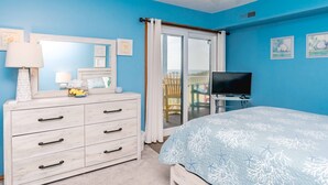 Quarto com cama, penteadeira, televisão e vista para uma varanda.