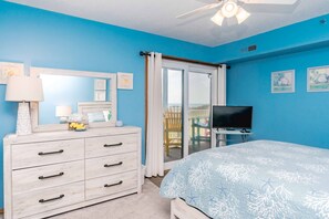 A bedroom with a bed, dresser, television, and a view of a balcony. - A Little Slice of Paradise on North Topsail Beach - 2BR Shipwatch Condo (North Topsail Beach)