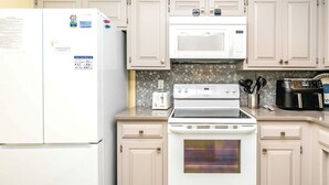 Cozinha com geladeira, micro-ondas, fogão e forno, tudo em branco.