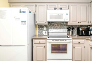 A kitchen with a white refrigerator, microwave, stove, and oven. - A Little Slice of Paradise on North Topsail Beach - 2BR Shipwatch Condo (North Topsail Beach)