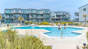 Piscina com área de lazer ao redor, cercada por um edifício residencial com varandas.