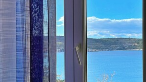 A window with a view of a body of water and a hilly landscape. - Apartment Neptun - seafront, 20 m from sea, sea view, terrace, private parking (Šilo)