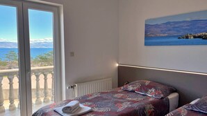A bedroom with a bed, a window with a view of the sea and mountains, and a painting on the wall.