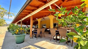 Eine Terrasse im Freien mit Holztischen und -stühlen, Blumentöpfen und einer überdachten Dachkonstruktion.