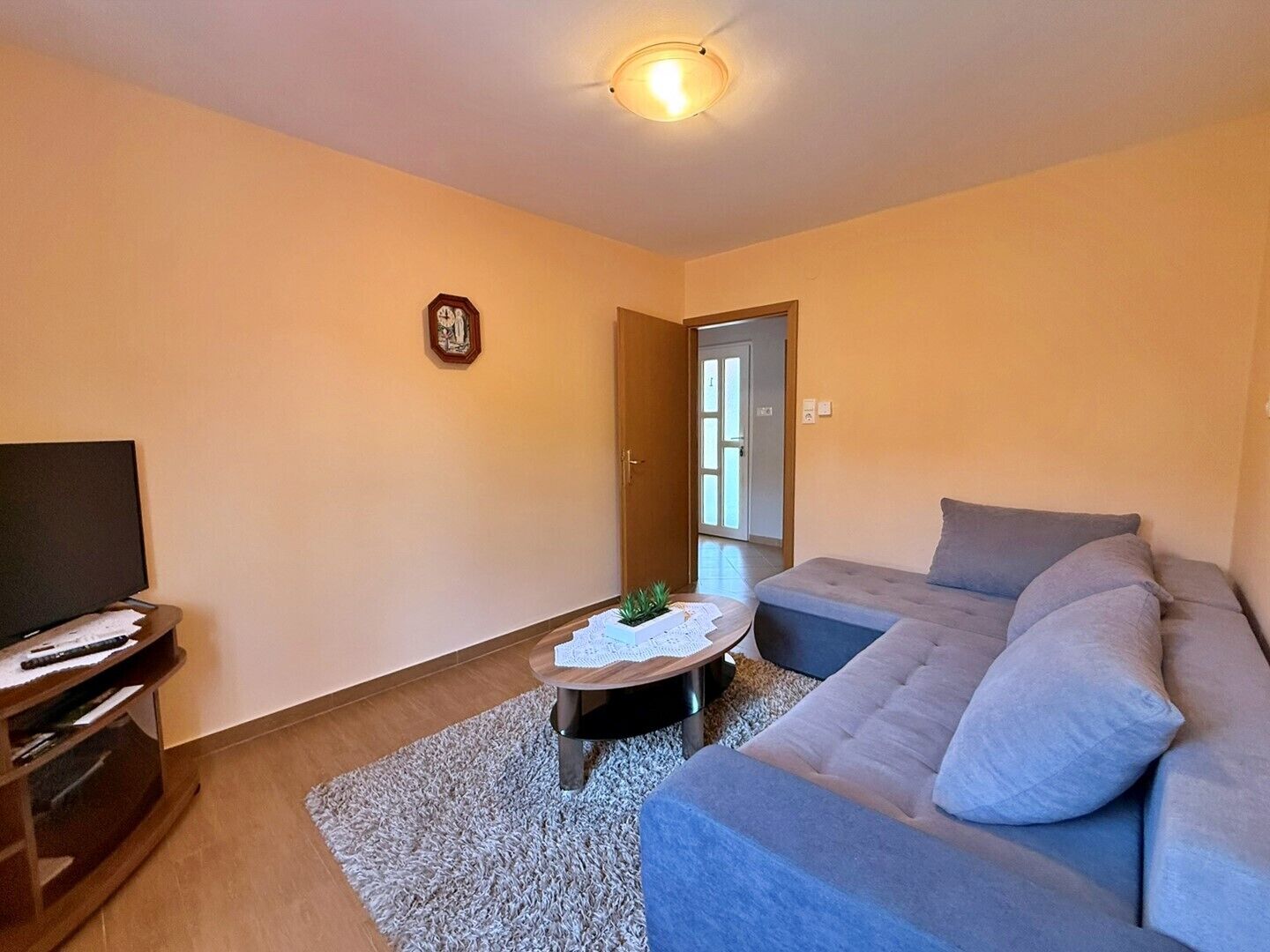 Una sala de estar con sofá, una mesa de centro, televisión y una puerta que da al exterior.