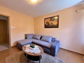 Ein Wohnzimmer mit einem Ecksofa, einem runden Couchtisch mit einer Pflanze und einem Gemälde an der Wand.