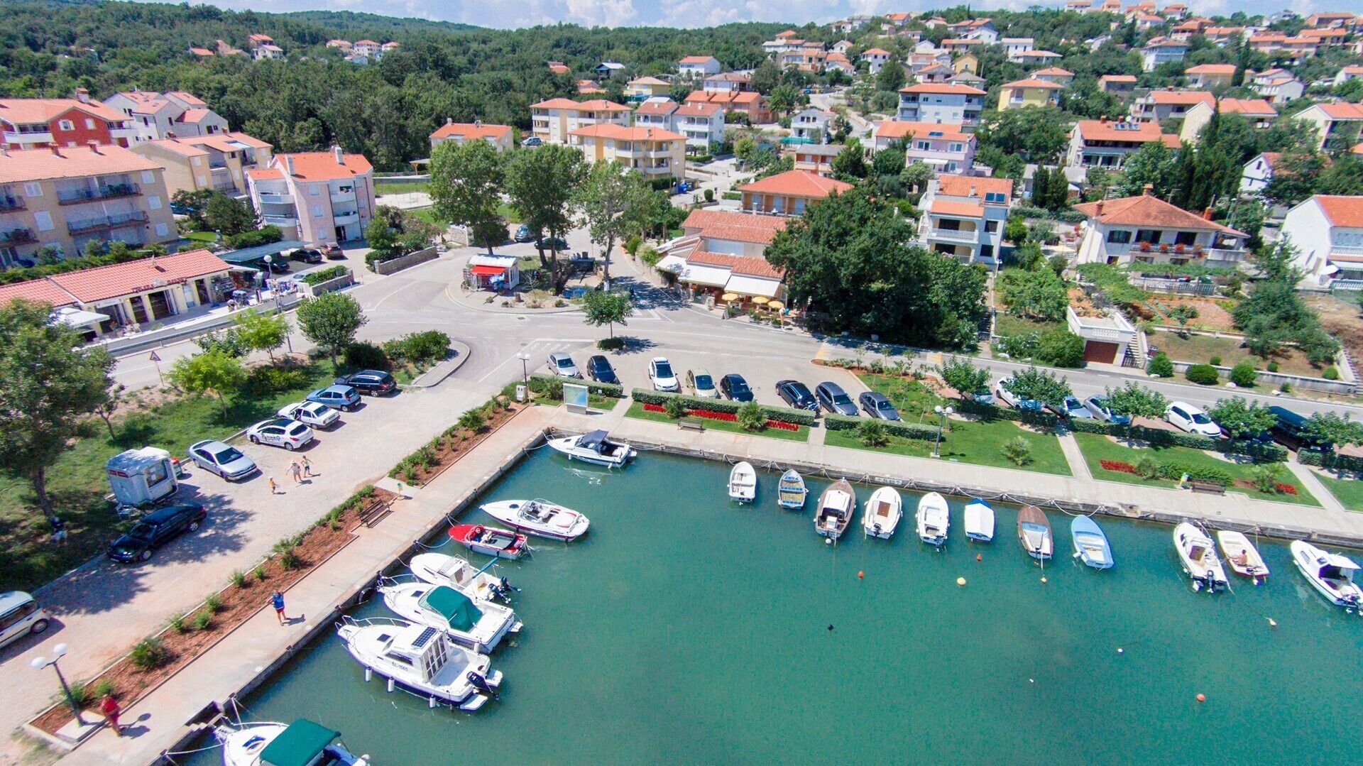 A marina with boats docked, surrounded by residential buildings with red-tiled roofs.