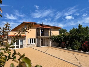Ein zweigeschossiges Haus mit Balkon, befestigter Auffahrt und umliegendem Grün.