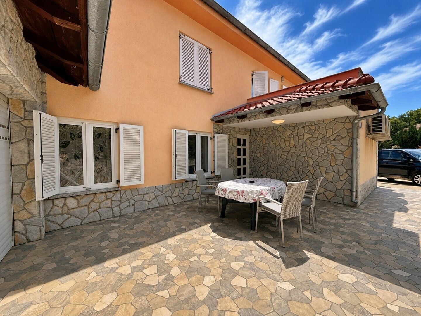 Un edificio rivestito in pietra con un patio piastrellato, posti a sedere all'aperto e persiane.