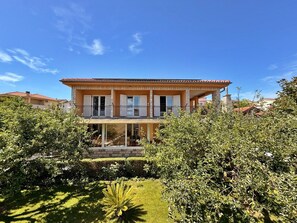 Une maison à deux étages dotée d’un balcon, entourée de verdure.