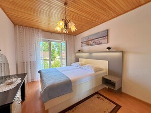 Una camera da letto con un letto, un comodino, una lampada da notte, una finestra con tende, un lampadario e una mensola a parete con un quadro.