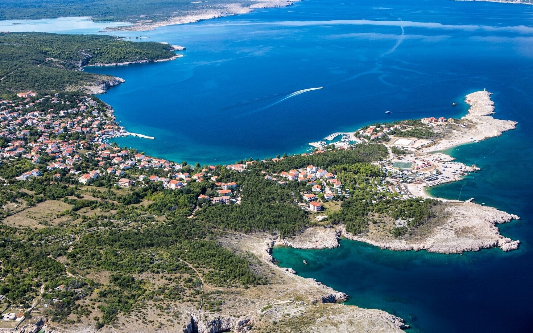 Luftaufnahme einer Küstenstadt mit Häusern, klarem, blauem Wasser und felsigem Gelände.