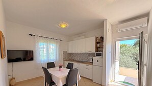 A modern kitchen with white cabinets, a dining table with chairs, a TV mounted on the wall, and a sliding glass door leading to a balcony.