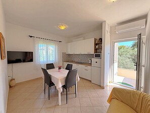 Una cucina moderna con mobili bianchi, un tavolo da pranzo con sedie, una TV a parete e una porta scorrevole in vetro che dà su un balcone.