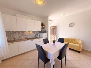 Una cucina compatta con mobili bianchi, uno schienale piastrellato, un forno a microonde e un tavolo con sedie.