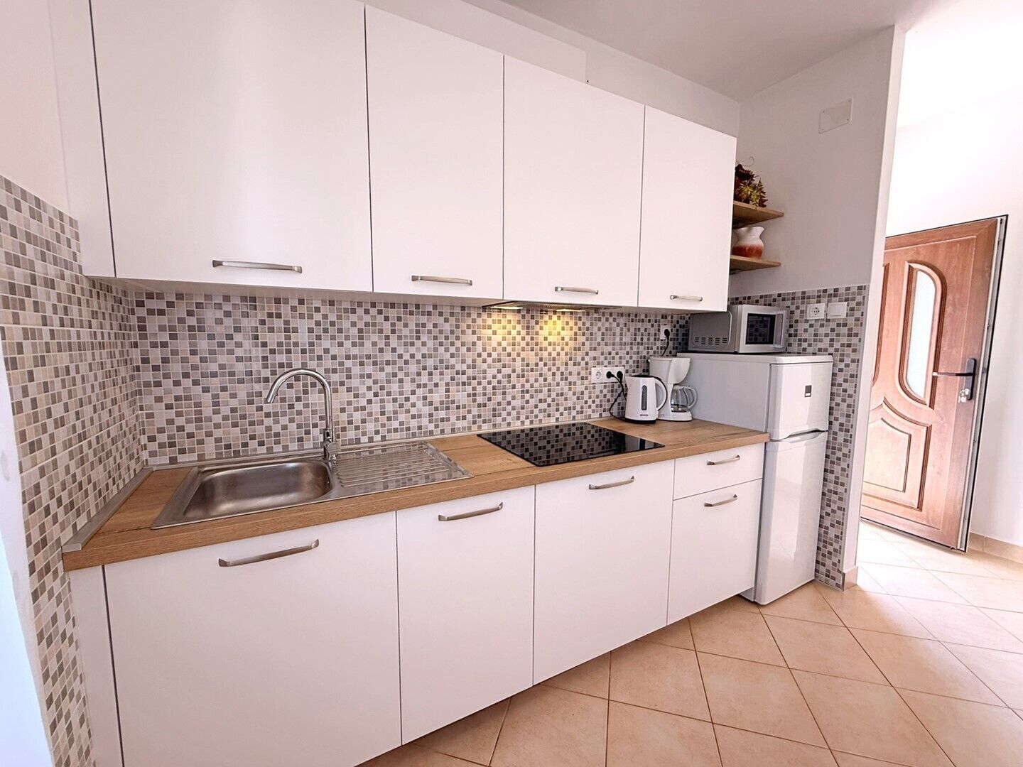 Una cucina con mobili bianchi, piastrelle a parete, lavello, fornello e microonde.
