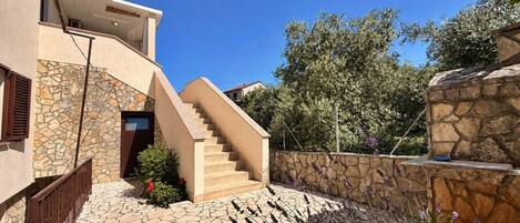 A modern building with a stone facade, a staircase leading to a door, and a stone wall with plants.