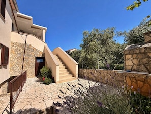 A modern building with a stone facade, a staircase leading to a door, and a stone wall with plants.