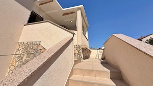 A modern building with a stone facade, a staircase leading to a covered area, and a clear blue sky.