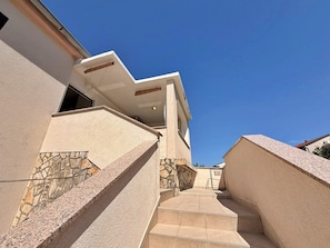A modern building with a stone facade, a staircase leading to a covered area, and a clear blue sky. - Apartment Nevenka - 130 m from sea and beach, sea view, balcony, terrace, BBQ (Šilo)